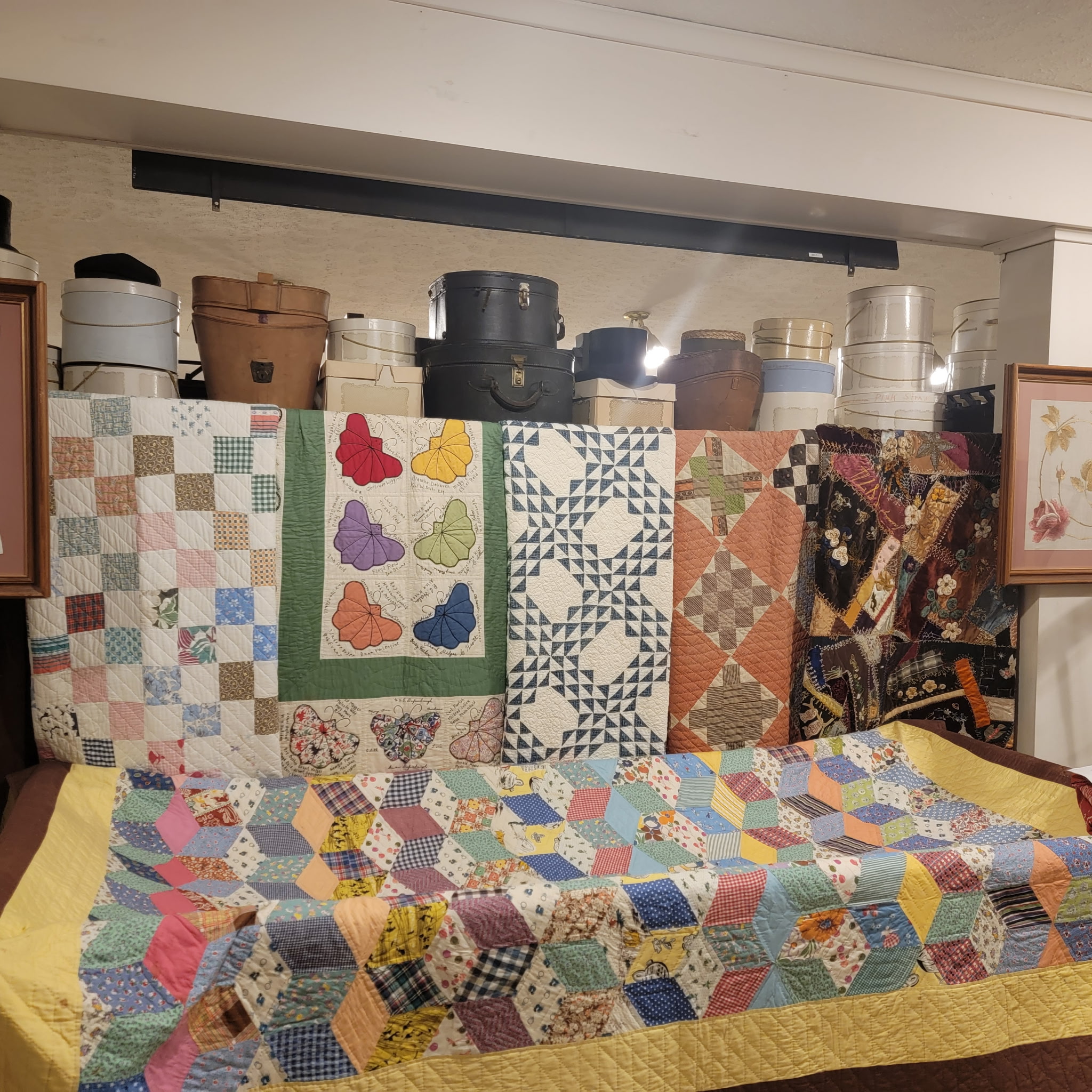 Antique quilts displayed beneath a row of vintage hat boxes