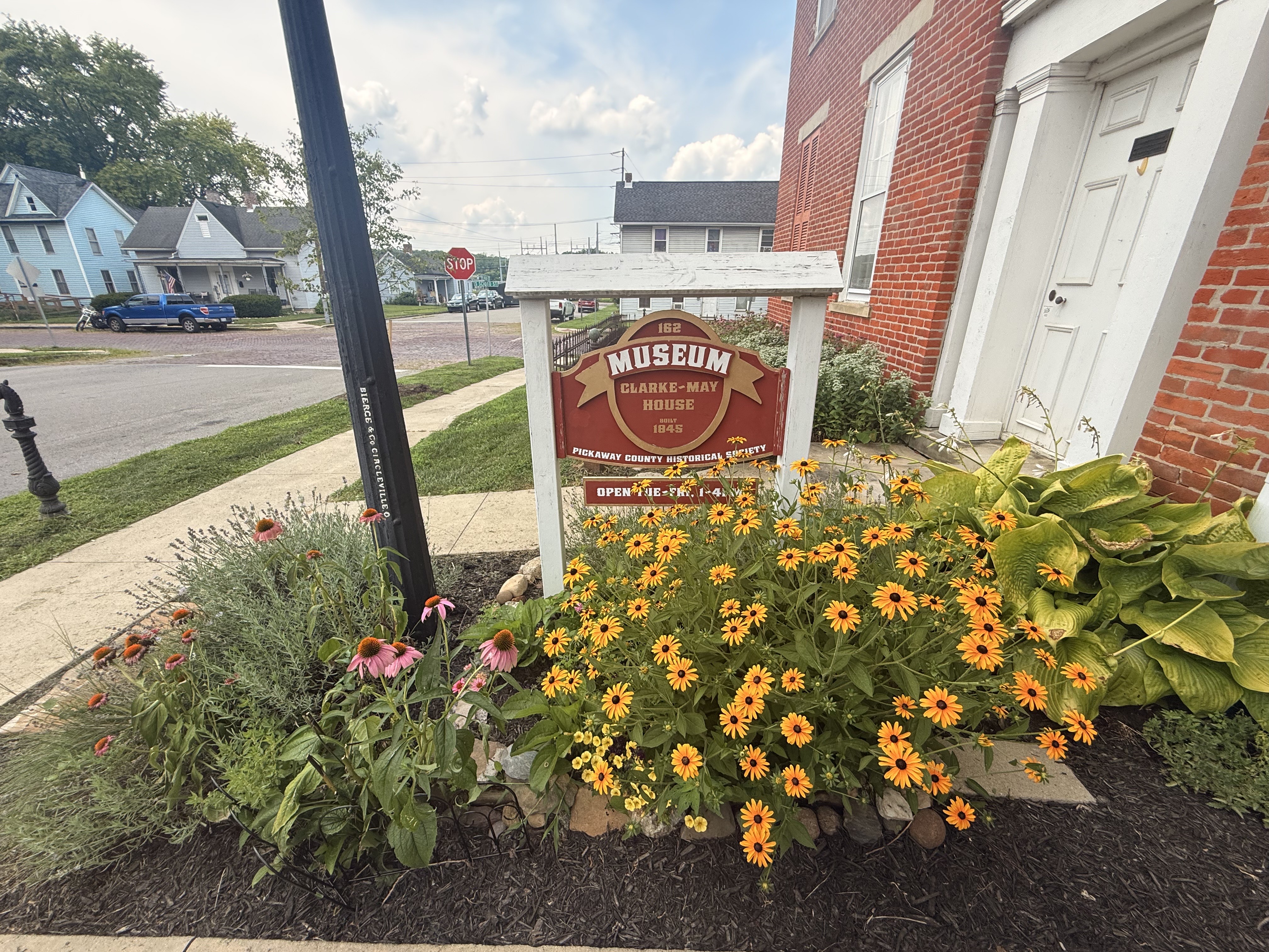 The Clarke-May House sign among black-eyed susans and hostas