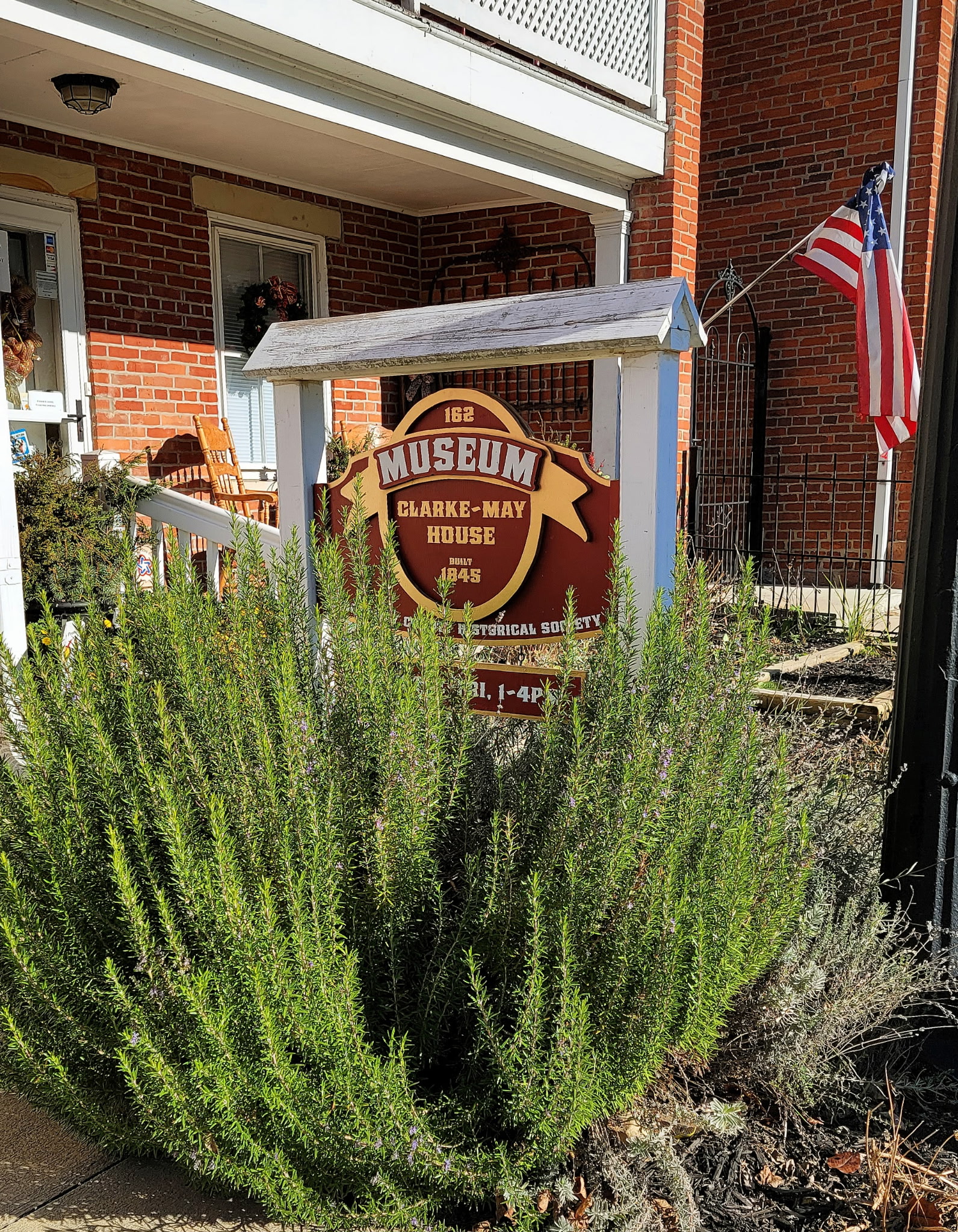 The Clarke-May House museum sign behind a large rosemary shrub