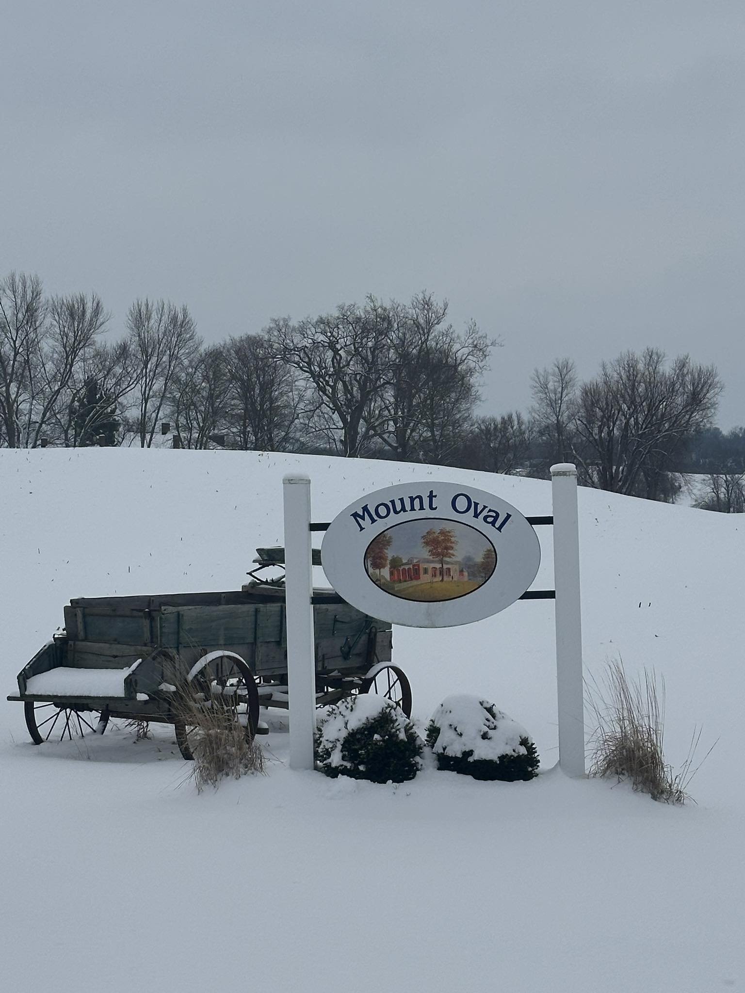 The Mount Oval sign and an antique wooden wagon in deep snow