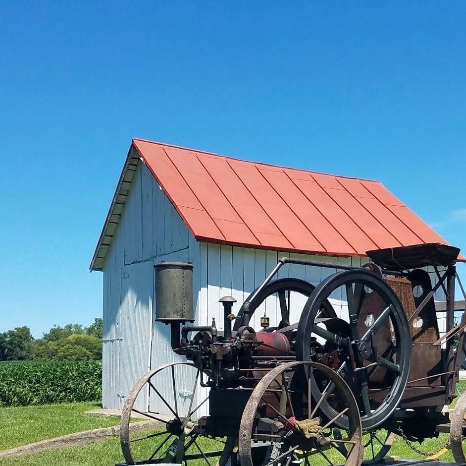 An antique steam engine parked beside a red-roofed barn